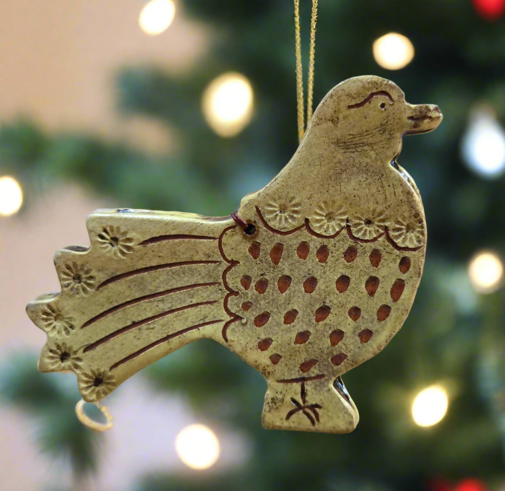 Decorative ceramic rooster ornament hanging against a blurred Christmas tree background.