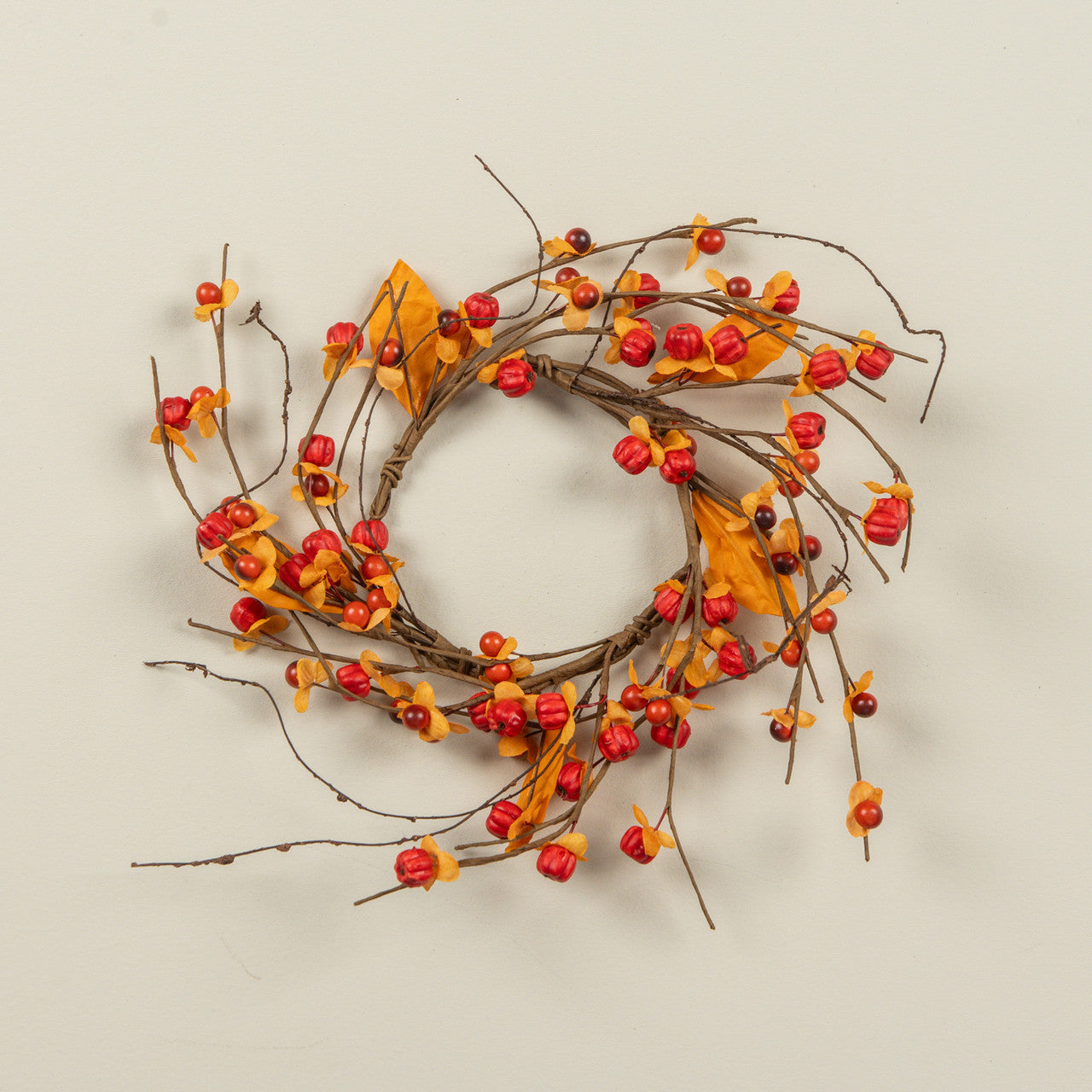 Decorative wreath with red berries and yellow leaves on a beige background