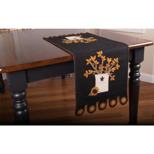 A black table runner with a floral design and decorative accents displayed on a wooden table.