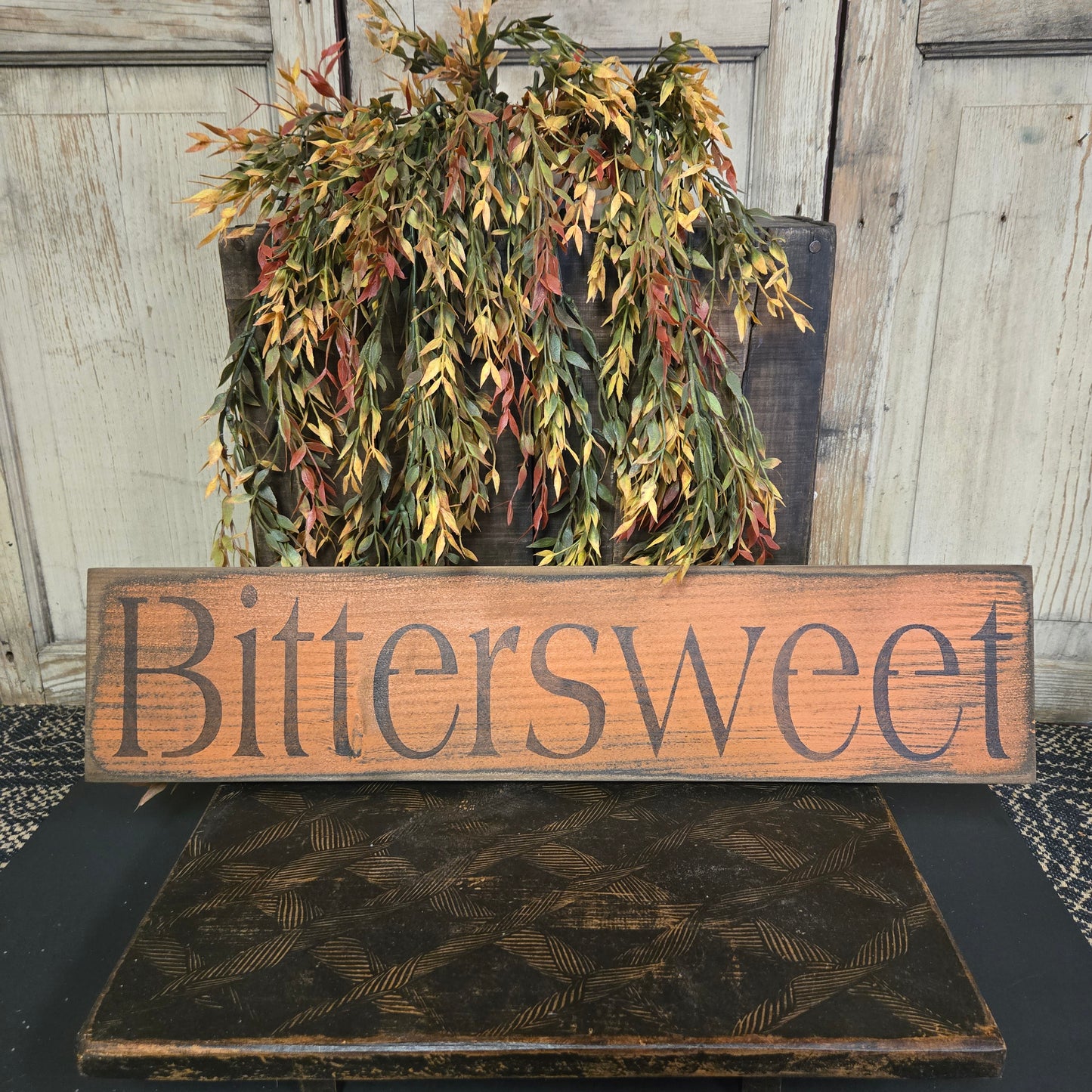 Wooden sign with 'Bittersweet' text next to a wreath on a door.