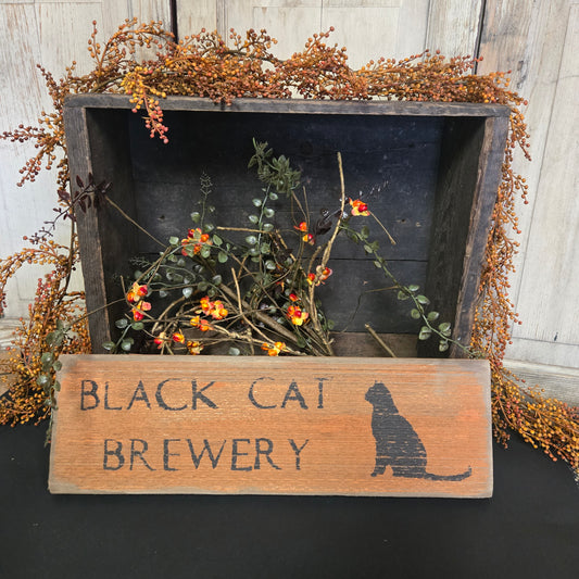 Decorative sign with 'Black Cat Brewery' on a wooden board with plants.