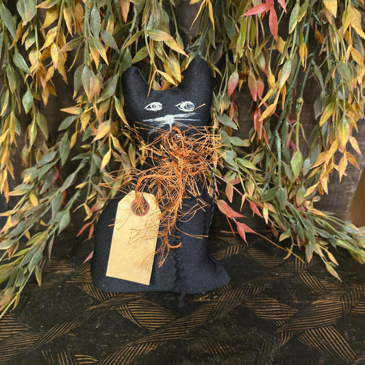 Black cat-shaped decoration with white face on a bed of green leaves