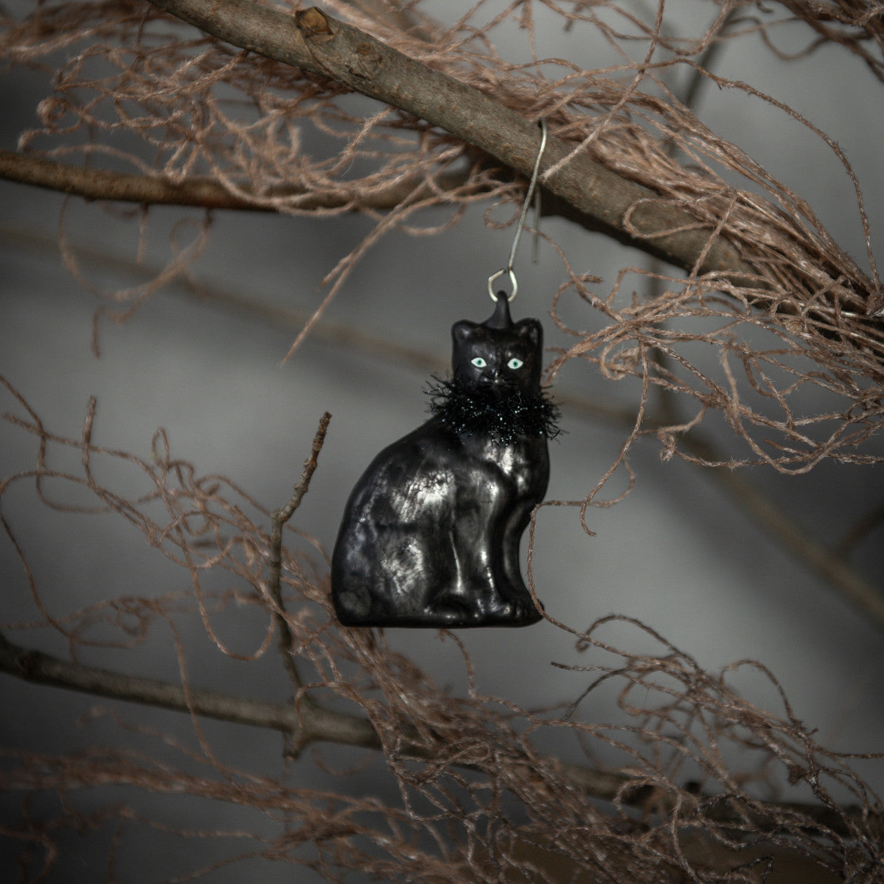 Black cat ornament hanging on a branch against a neutral background