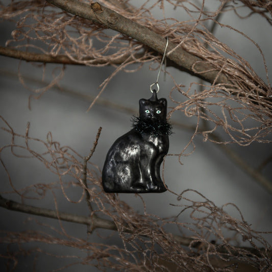Black cat ornament hanging on a branch against a neutral background