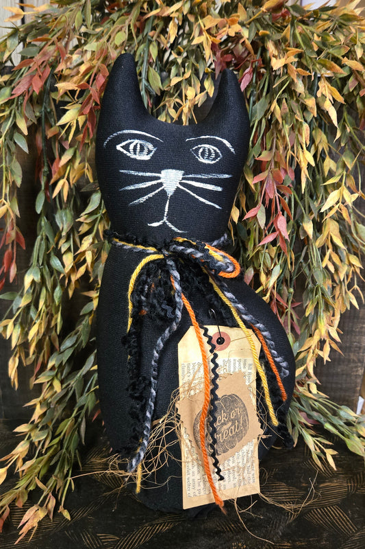 Black cat-shaped decoration with white face details against a leafy background
