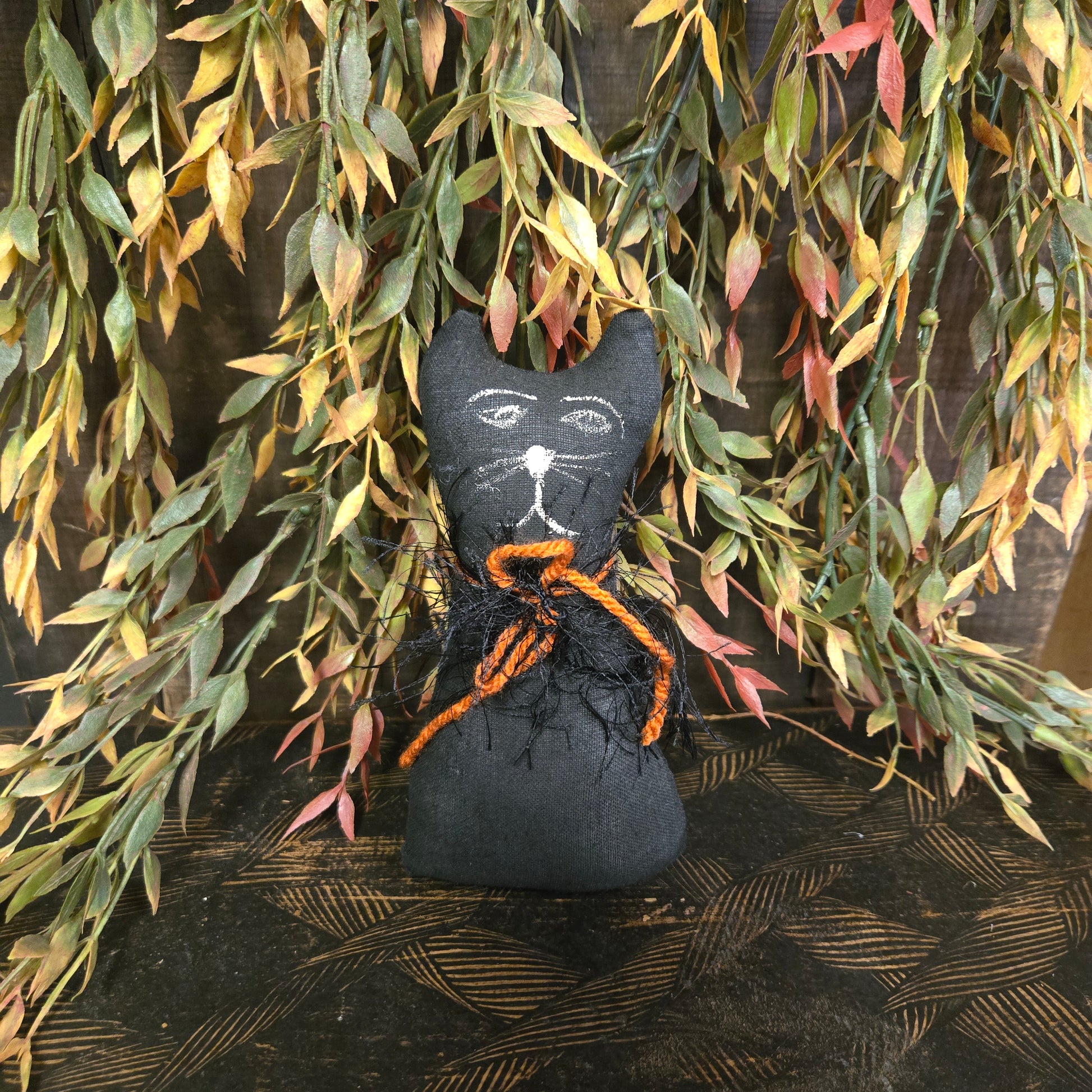 Black cat-shaped decoration with orange accents on a leafy background