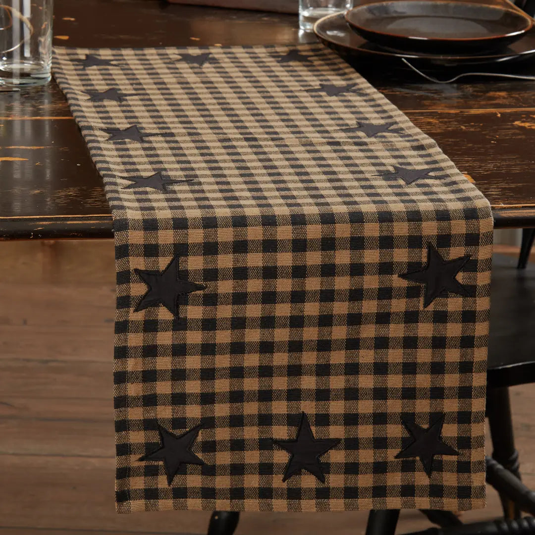 A rustic brown and beige buffalo check table runner with black embroidered stars, displayed on a dark wooden dining table.