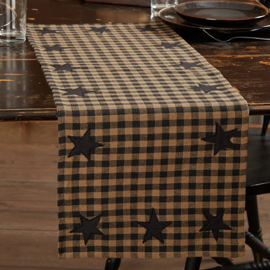 A rustic brown and beige buffalo check table runner with black embroidered stars, displayed on a dark wooden dining table.