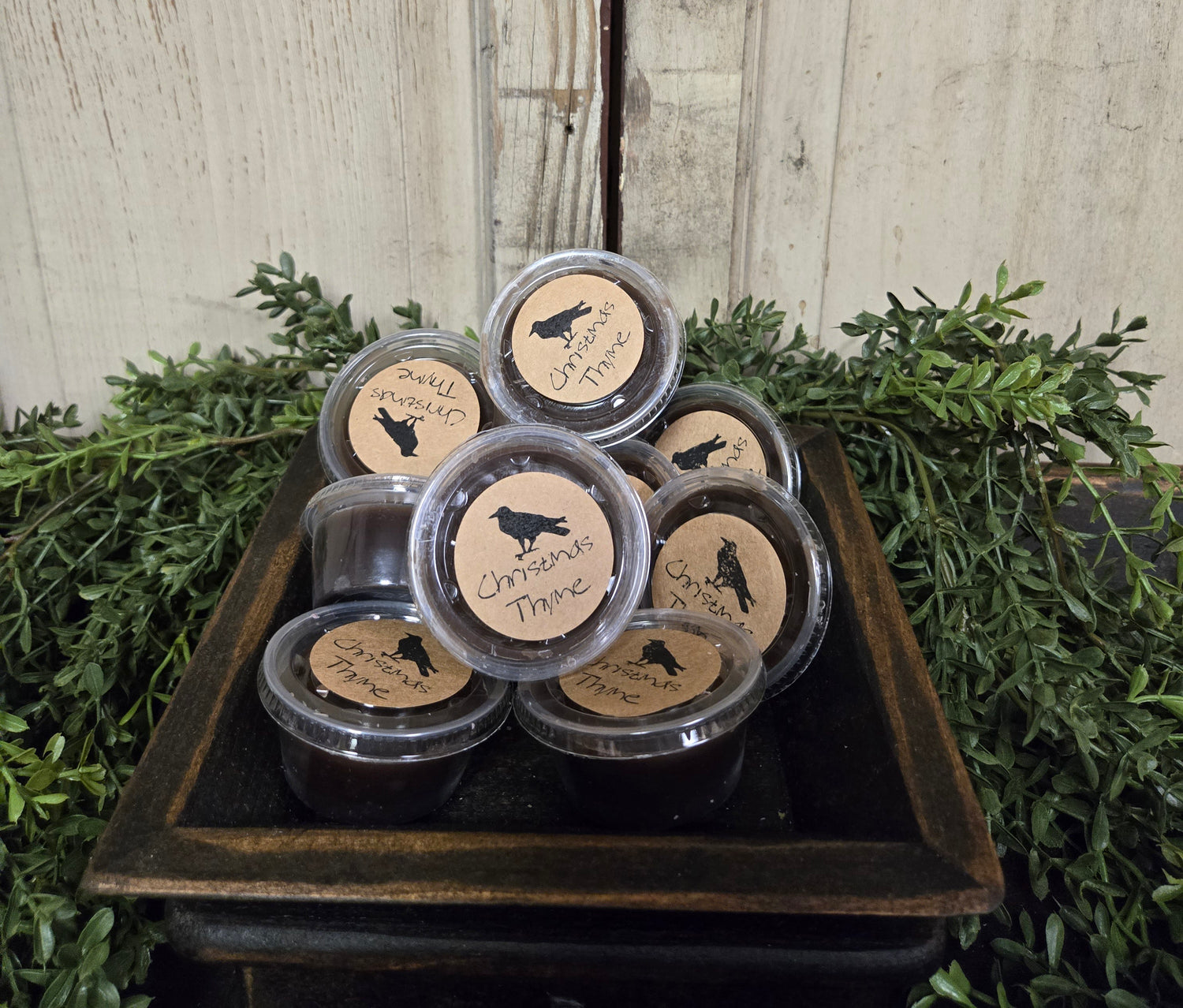 A collection of Black Crow Wax Tarts displayed in a tart warmer, surrounded by greenery.