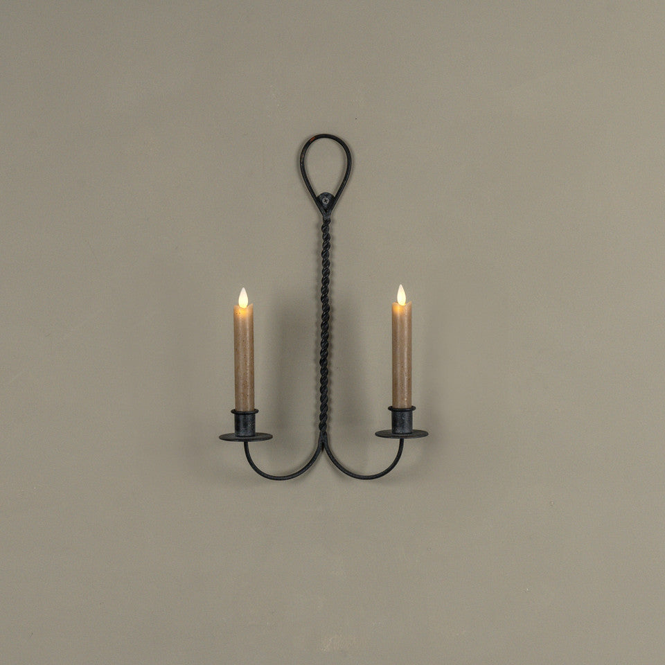 Wrought iron wall sconce with two lit candles on a beige wall