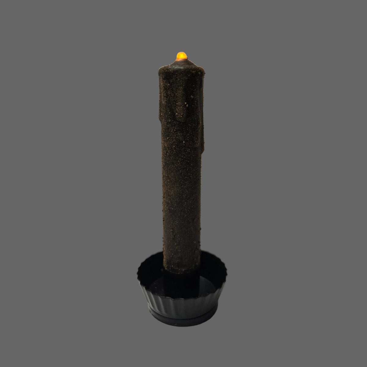 A dark brown textured candle with a black base, photographed against a white corrugated cardboard background.