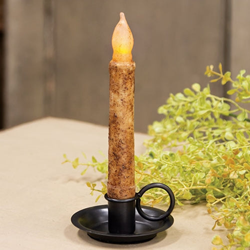 Decorative candle with a lit wick on a black holder, surrounded by greenery.