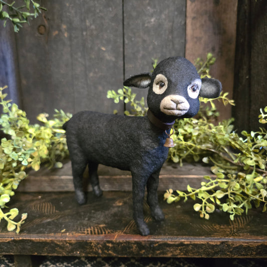 Black sheep figurine in front of a wooden surface with green foliage