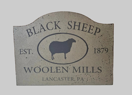 Decorative sign for Black Sheep Woollen Mills with a sheep silhouette and establishment year on a light gray background.