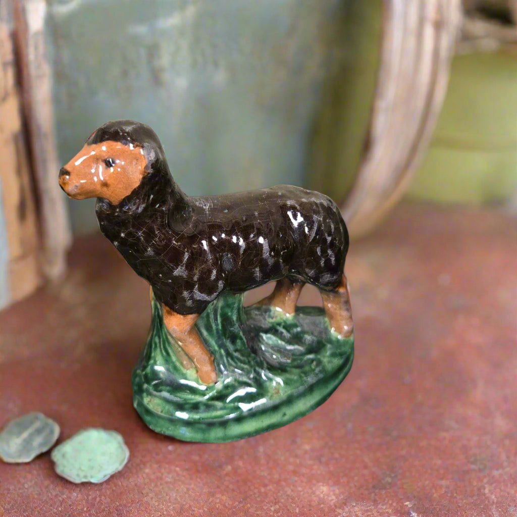Pottery sculpture of a black sheep on a wooden surface with greenery