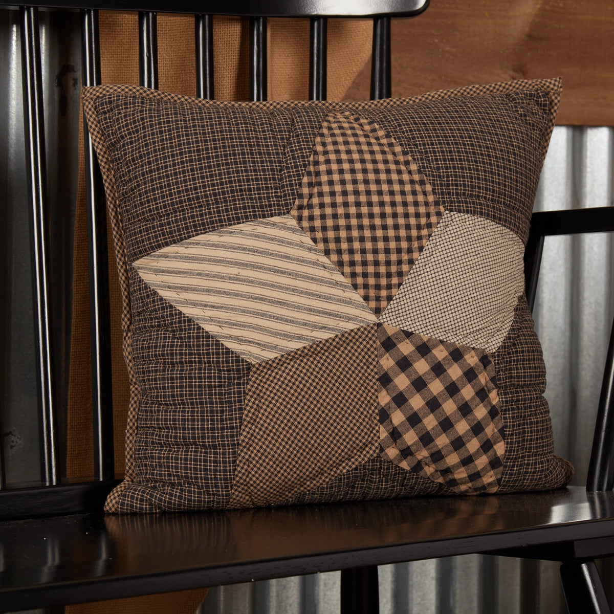 Black and tan farmhouse pillow with a five-point patchwork star, resting on a black wooden bench.