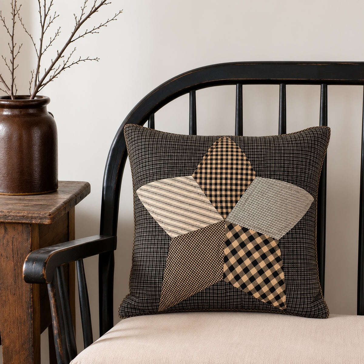 Black and tan patchwork star pillow with checked and striped fabrics, displayed on a cushioned black wooden chair.