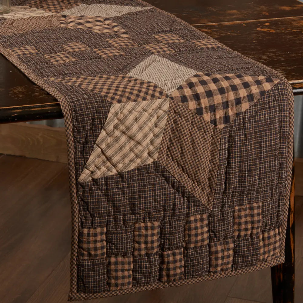 Black and tan quilted table runner draped over a wooden table, featuring patchwork stars and checkerboard accents.