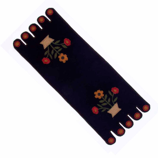 A black table runner with a floral design in mustard and red colors, featuring embroidered flowers and a fringed edge.