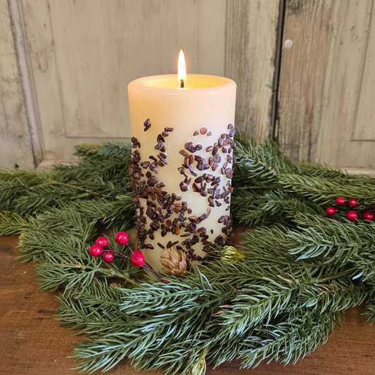 Decorative candle with speckles on a bed of greenery and berries against a wooden background