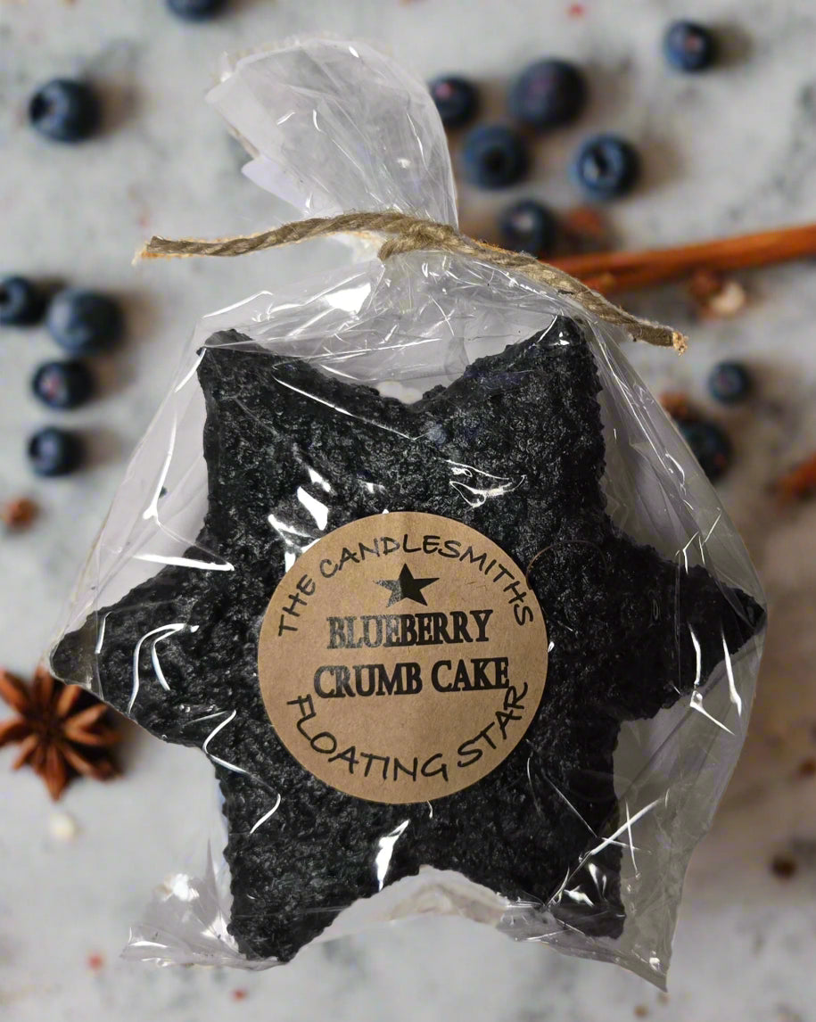 A packaged floating candle shaped like a star, labeled 'The Blueberry Crumb Cake' with branding from 'The Candlesmiths'.