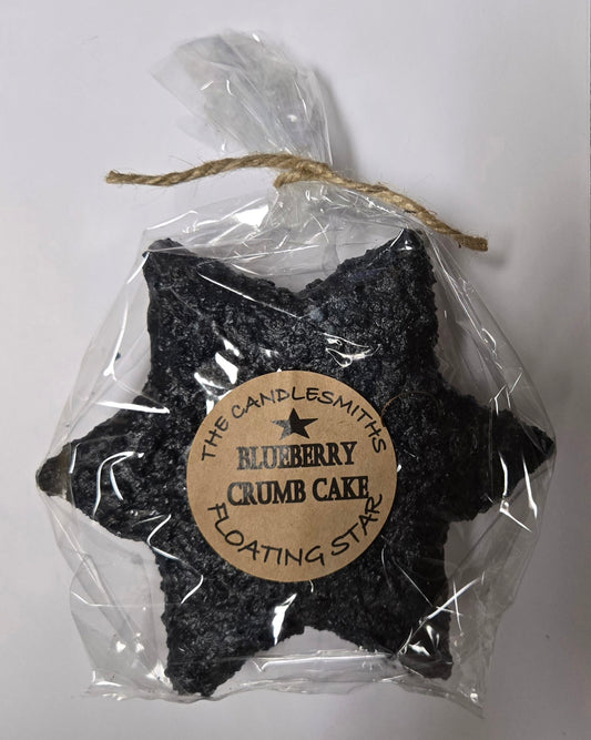A packaged floating candle shaped like a star, labeled 'The Blueberry Crumb Cake' with branding from 'The Candlesmiths'.