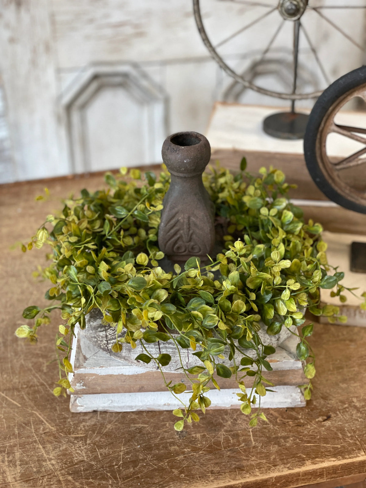 Decorative arrangement with greenery and a small vase on a wooden surface.
