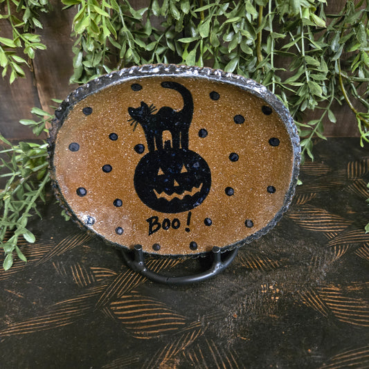 Decorative pottery with a black cat silhouette and 'Boo!' text on a brown background, surrounded by greenery.
