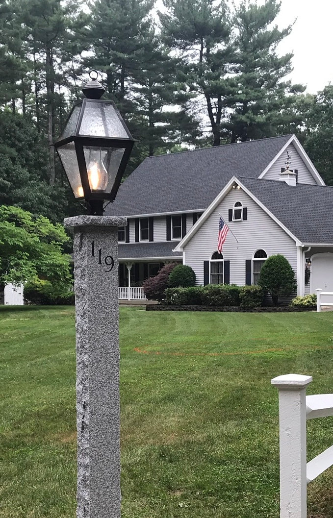 Post light in a yard next to a fence and in front of a house with a flag.