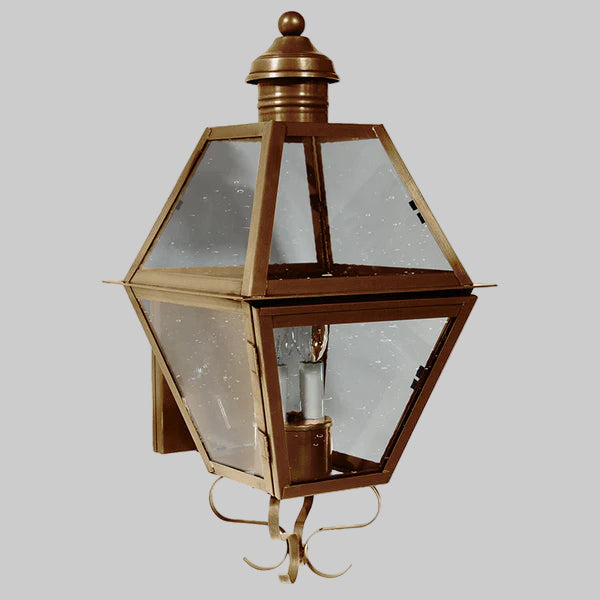 Decorative outdoor wall light fixture with brass finish and clear glass on a gray background
