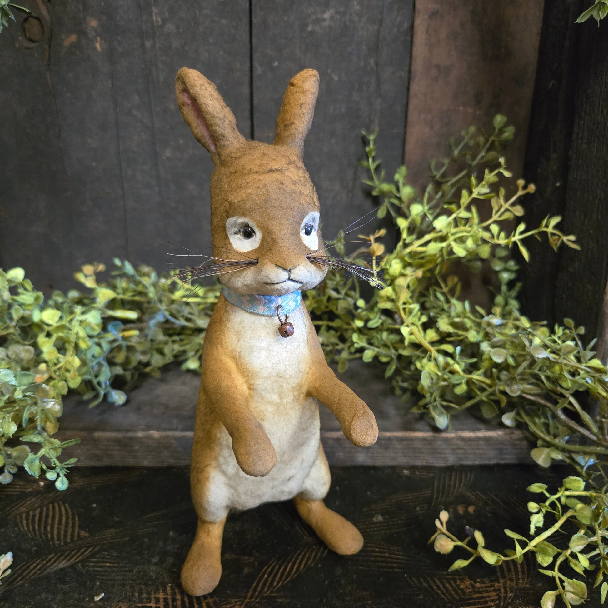 Paper mache rabbit figure on a wooden background with greenery