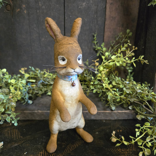 Paper mache rabbit figure on a wooden background with greenery