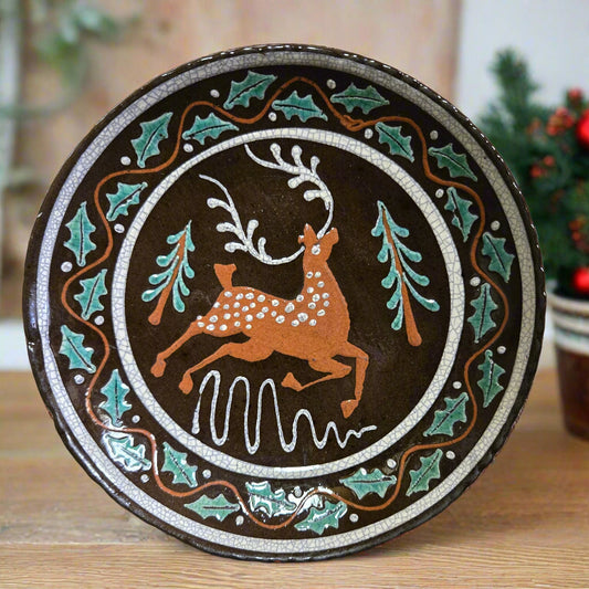 A handcrafted ceramic plate with a turtle creek pottery design featuring a deer in the center, surrounded by a brown, green, and white pattern.
