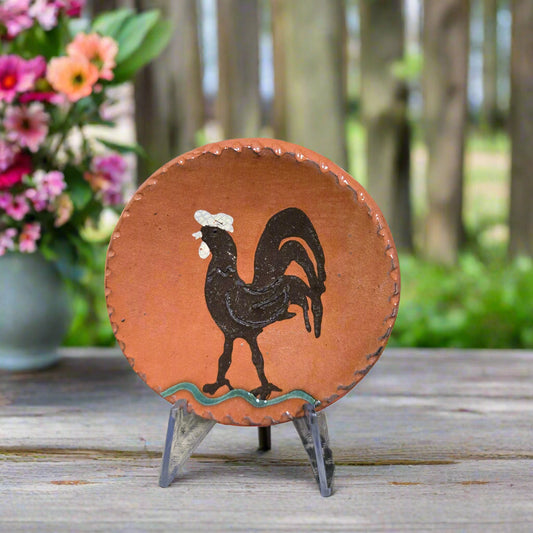 Small round redware plate with a brown rooster standing on grass