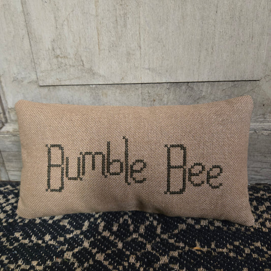 Beige pillow with 'Bumble Bee' text on a textured surface.