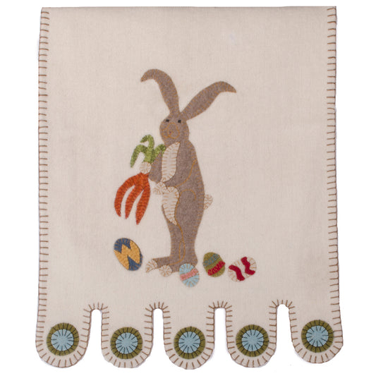 A beige table runner with an embroidered design of a rabbit and colorful eggs at the bottom.