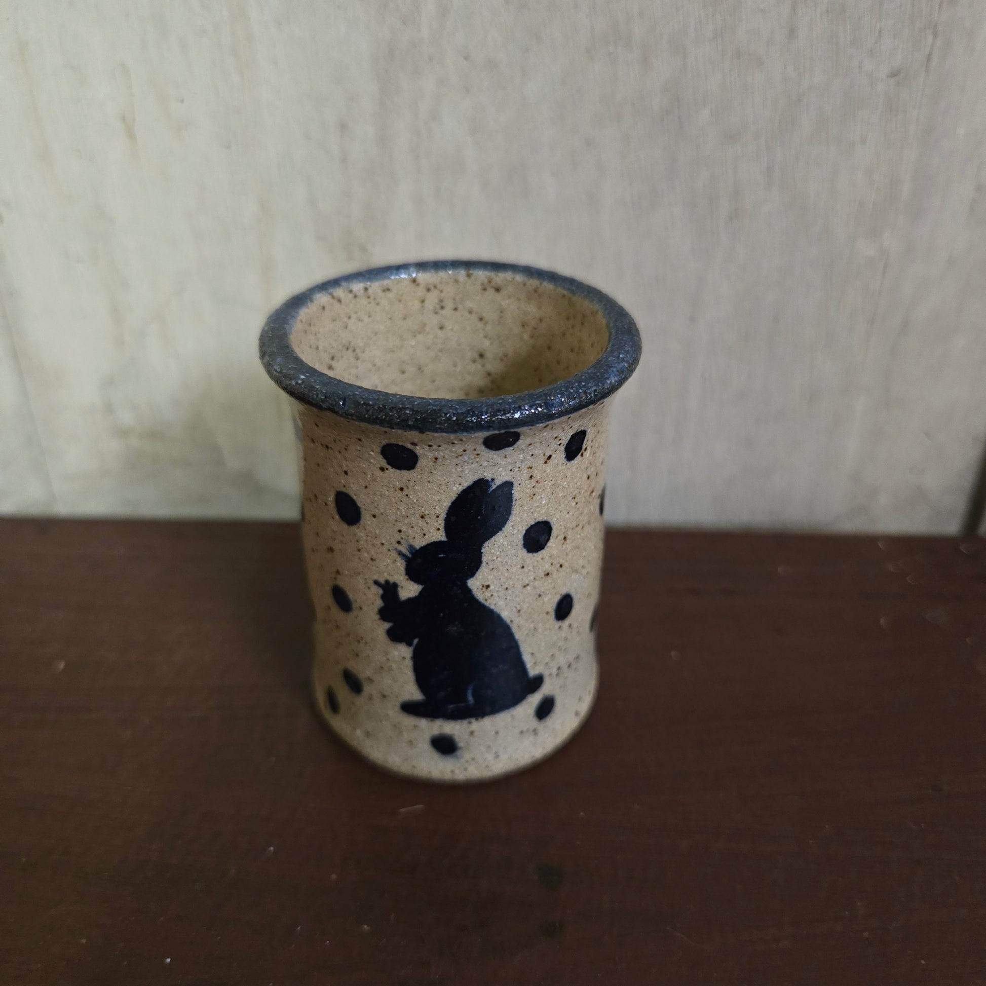 Ceramic container with black speckles and a bunny design on a wooden surface
