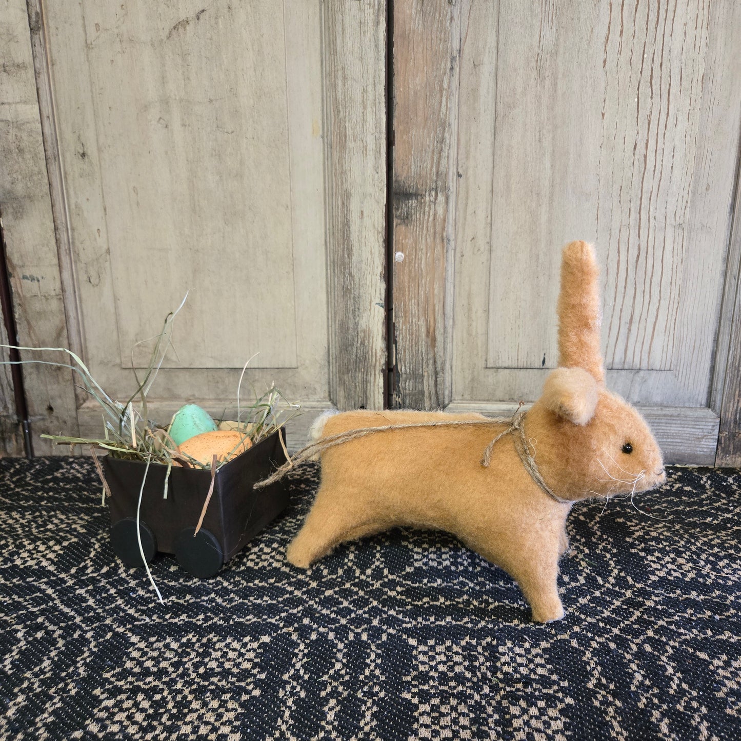 A hand-made brown cart with a cute bunny pulling a load of colorful Easter eggs, positioned against a wooden backdrop.