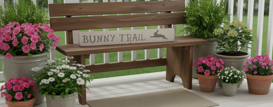 Wooden bench with 'Bunny Trail' sign surrounded by potted flowers on a patio.