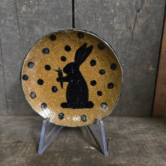 Decorative plate with a black rabbit silhouette on a gold polka dot background, attached to a wooden surface.