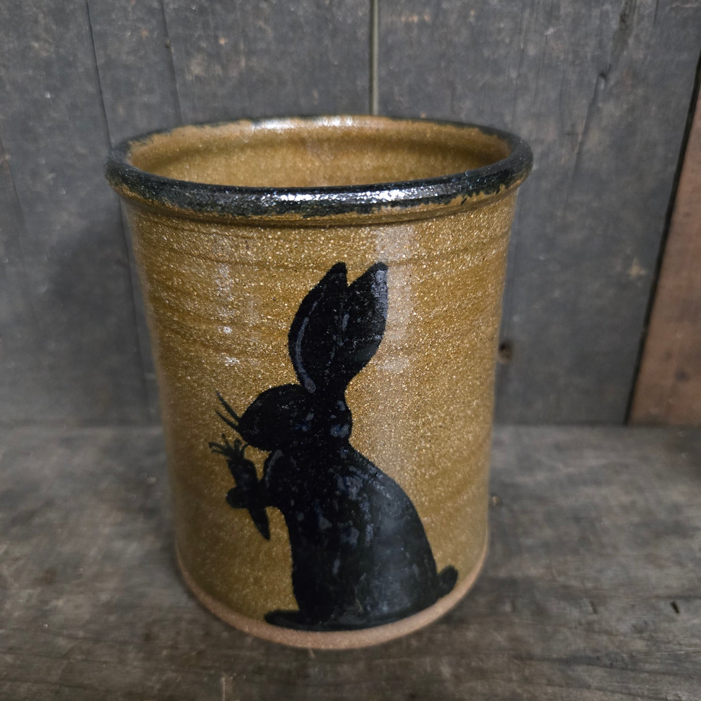 Cylindrical ceramic object with a black silhouette of a bunny on a textured surface