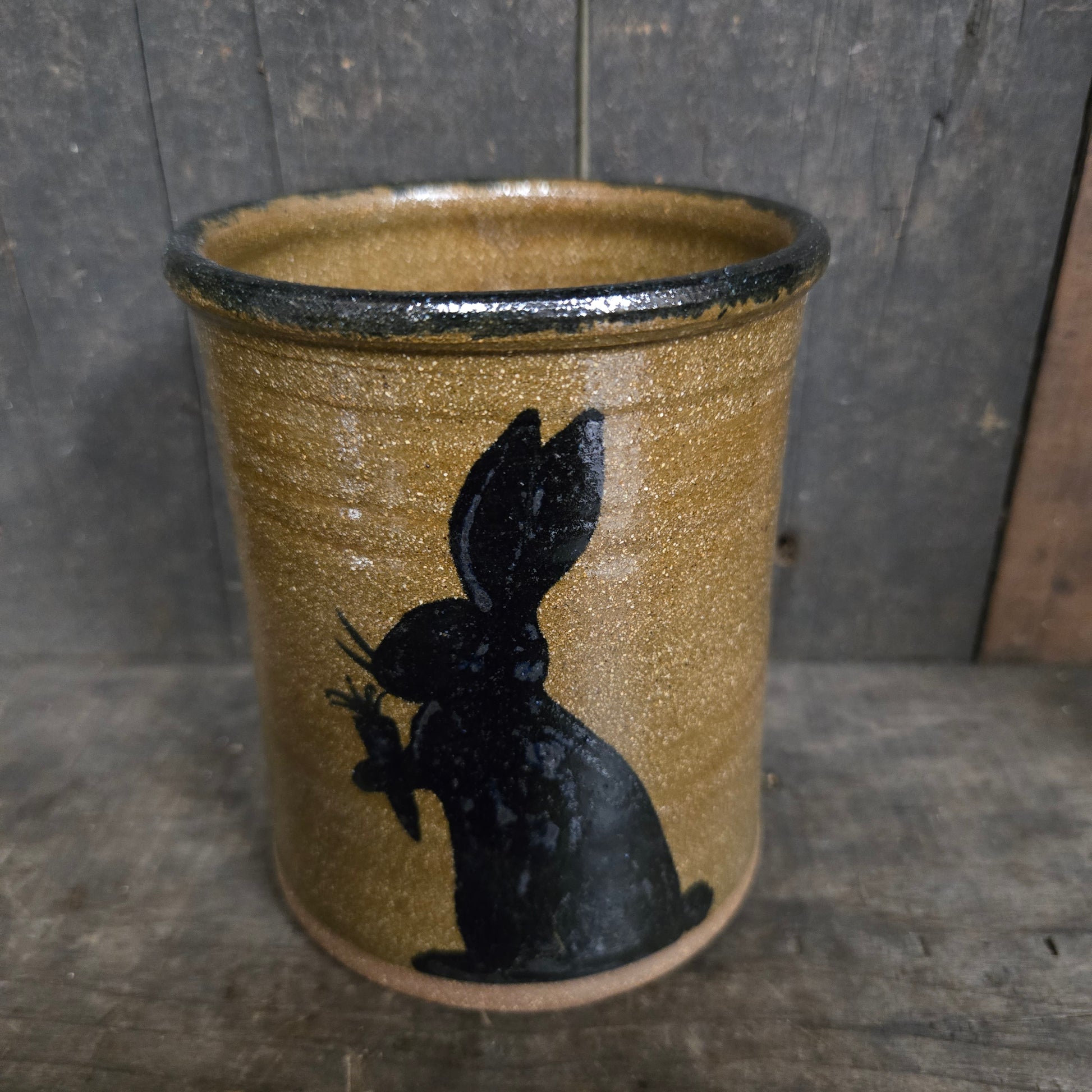 Cylindrical ceramic object with a black silhouette of a bunny on a textured surface