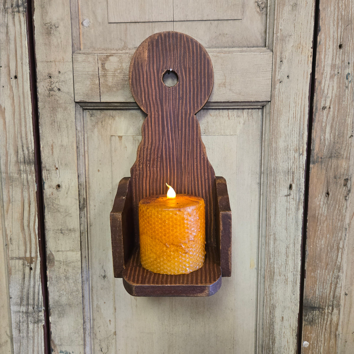 A rustic wooden wall sconce mounted on a door, holding a lit candle, with visible wood grain and craftsmanship.