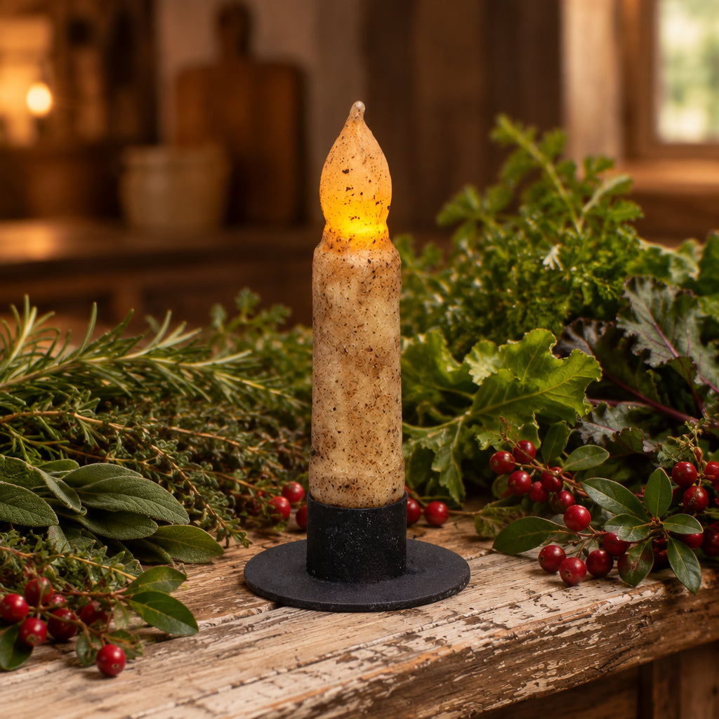 Decorative candle with a glowing yellow tip on a wooden surface with flowers in the background