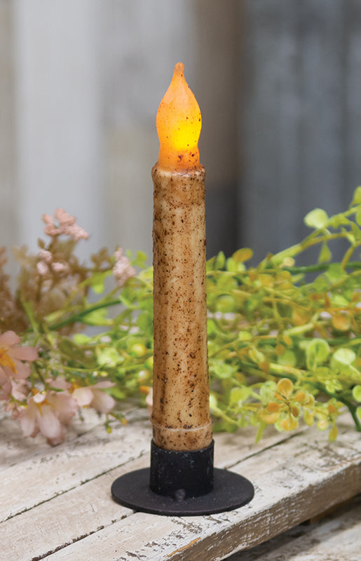 Decorative candle with flame on a wooden surface with flowers and leaves in the background