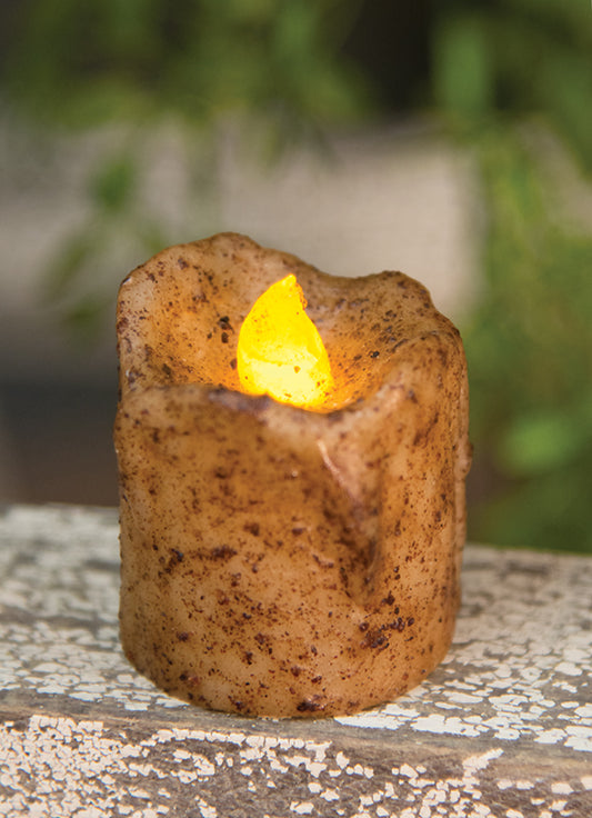 A burnt ivory mini drip timer votive candle with an orange flame, placed on a textured surface.