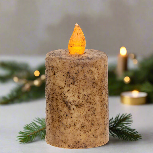 Decorative candle with a small orange candle on top, surrounded by greenery and lights.
