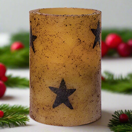 A cylindrical pillar candle with a burnt ivory color and multiple black stars pattern on it.