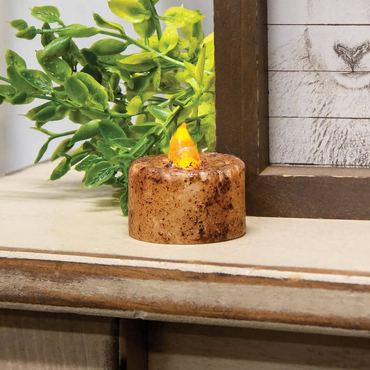 Small decorative candle with a flame on a wooden surface next to a plant