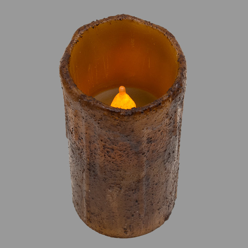 Cylindrical candle with textured surface and orange flame on a gray background